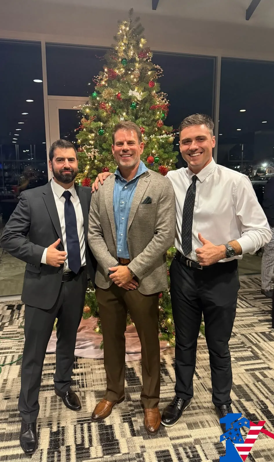 Mike, Byron and Max stand in front of a lit Christmas tree, Mike and Max giving a thumbs-up.
