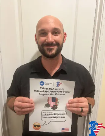 John smiles holding a 1 Vision USA flyer that says it supports our veterans.