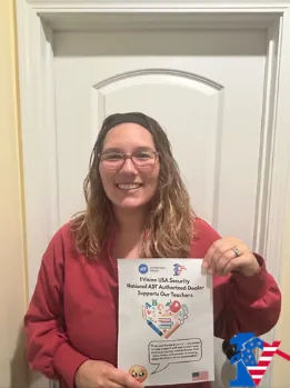 Katie smiles holding a 1 Vision USA flyer that says it supports our teachers.