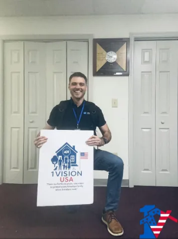 Max kneels and smiles, holding a 1 Vision USA sign in front of white closet doors.