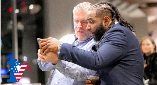 Two men lean in together to look at a phone at the holiday party.