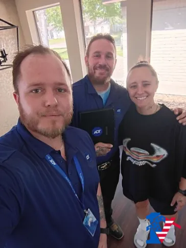Three people smile in a selfie in a bright living room; one holds an ADT tablet.