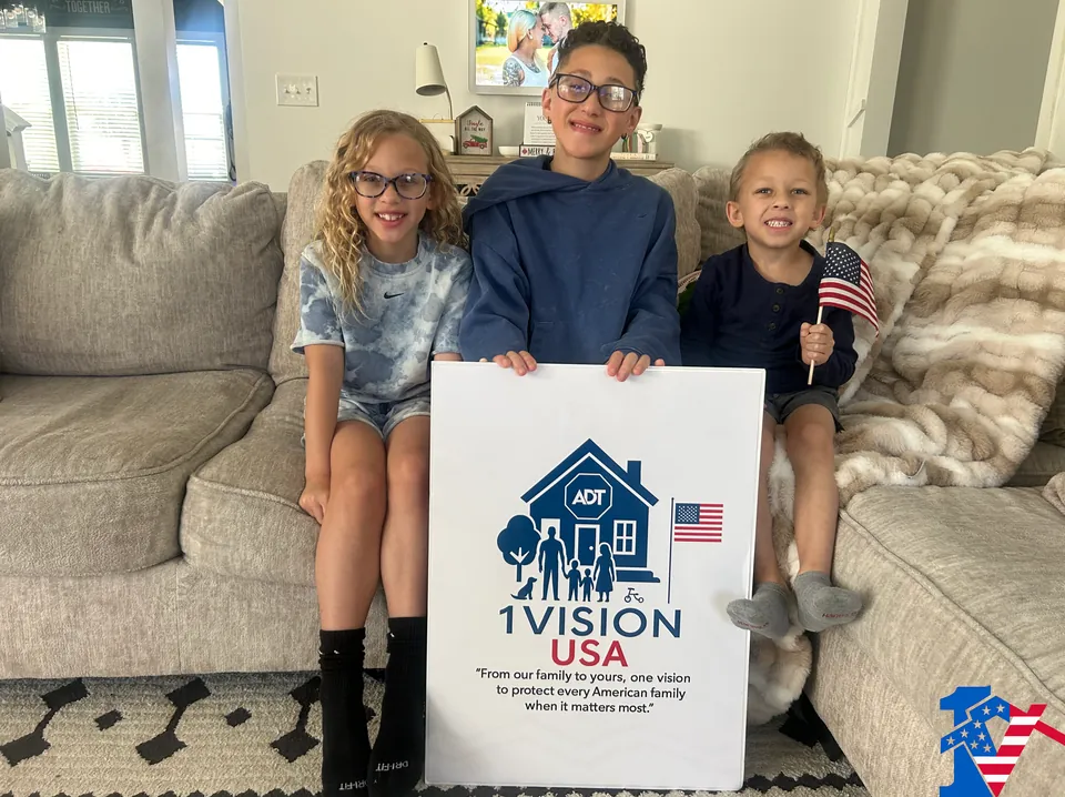 Seth's three children sit on a couch holding a 1 Vision USA sign; the youngest waves a small flag.