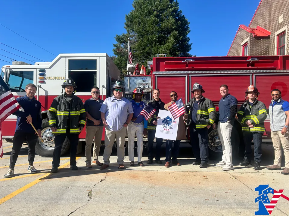 The team and firefighters in gear line up in front of a red Columbia fire engine with flags and a sign.