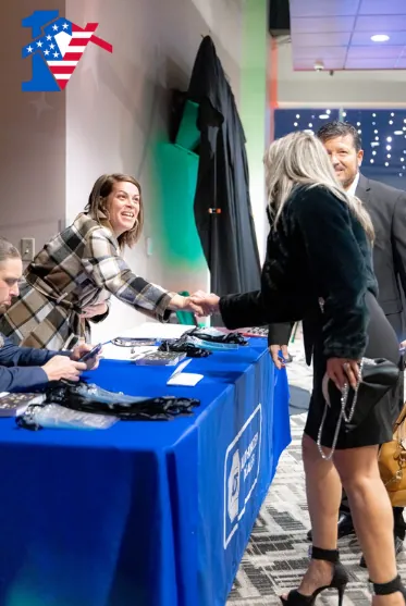 Terri, at a blue check-in table, smiles and shakes hands with a guest at the holiday party.